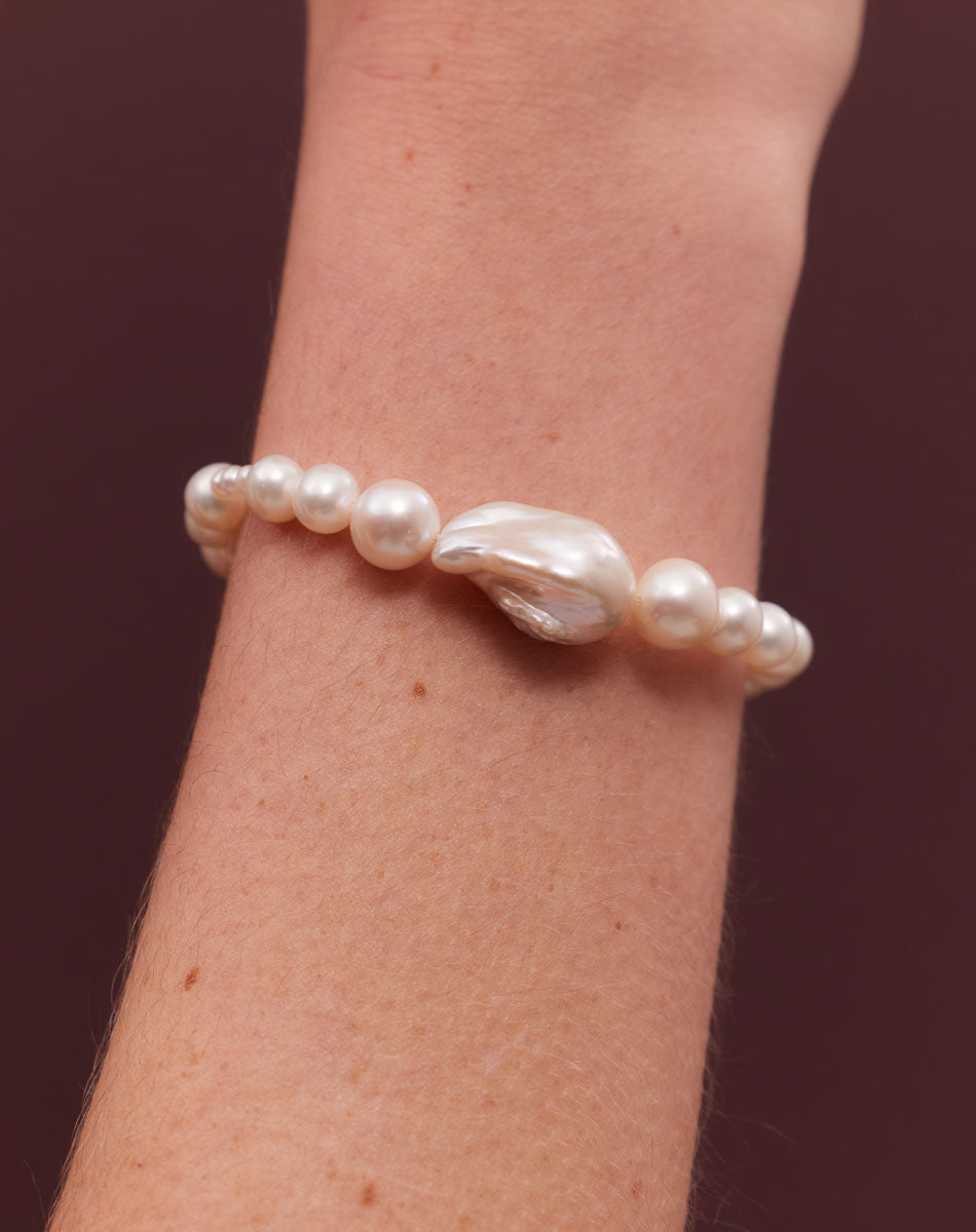 A pearl bracelet featuring a string of round and baroque pearls worn on a wrist