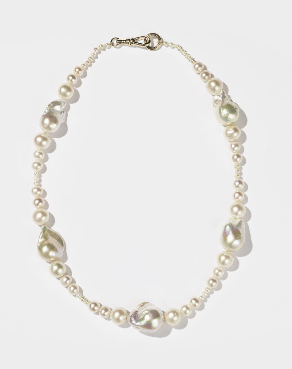 A string of round and baroque pearls with a gold clasp, designed to drape across the collarbone.