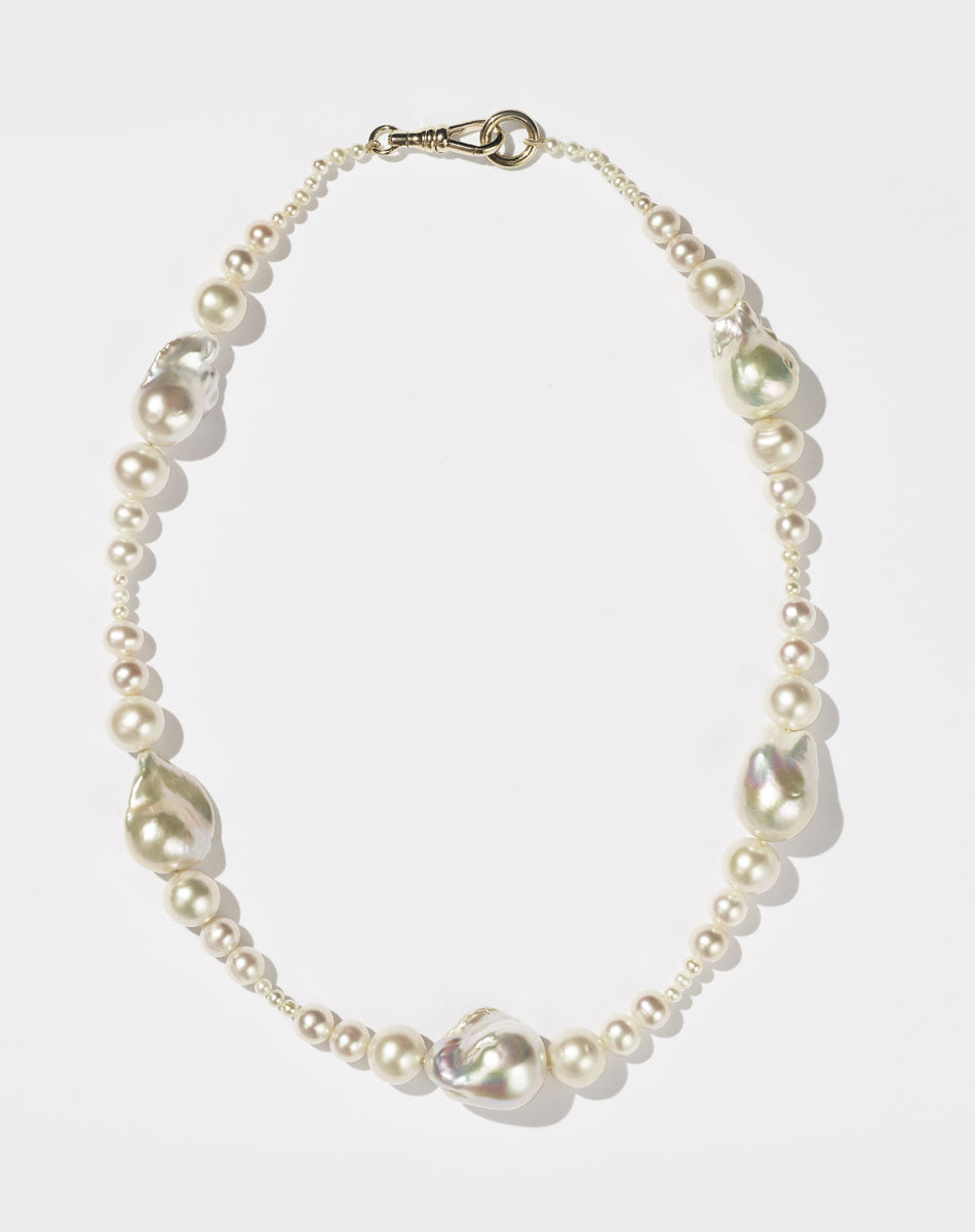 A string of round and baroque pearls with a gold clasp, designed to drape across the collarbone.