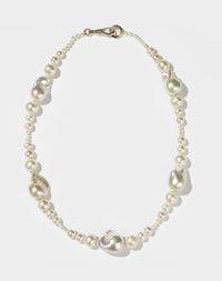 A string of round and baroque pearls with a gold clasp, designed to drape across the collarbone.
