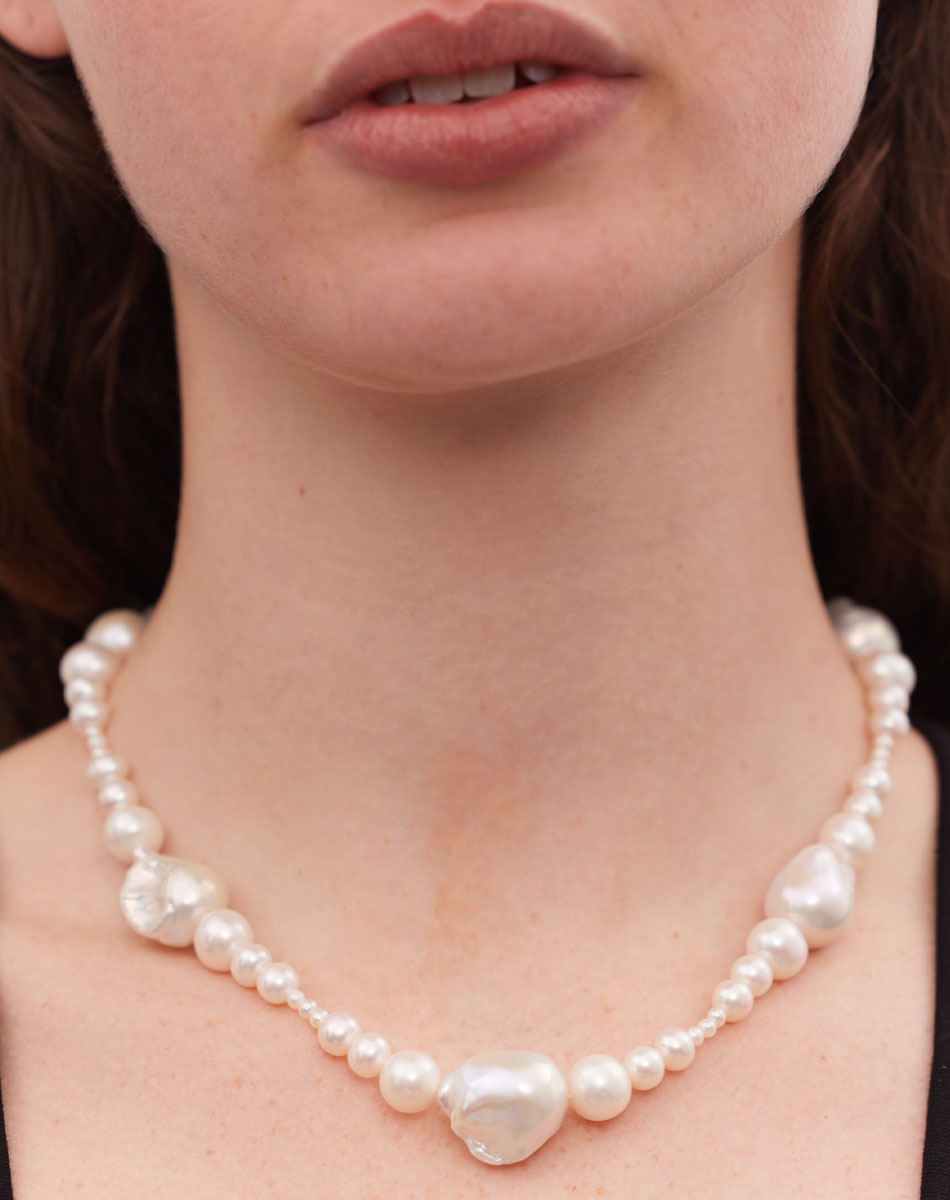 A necklace featuring a strand of round and baroque freshwater pearls worn on a model.