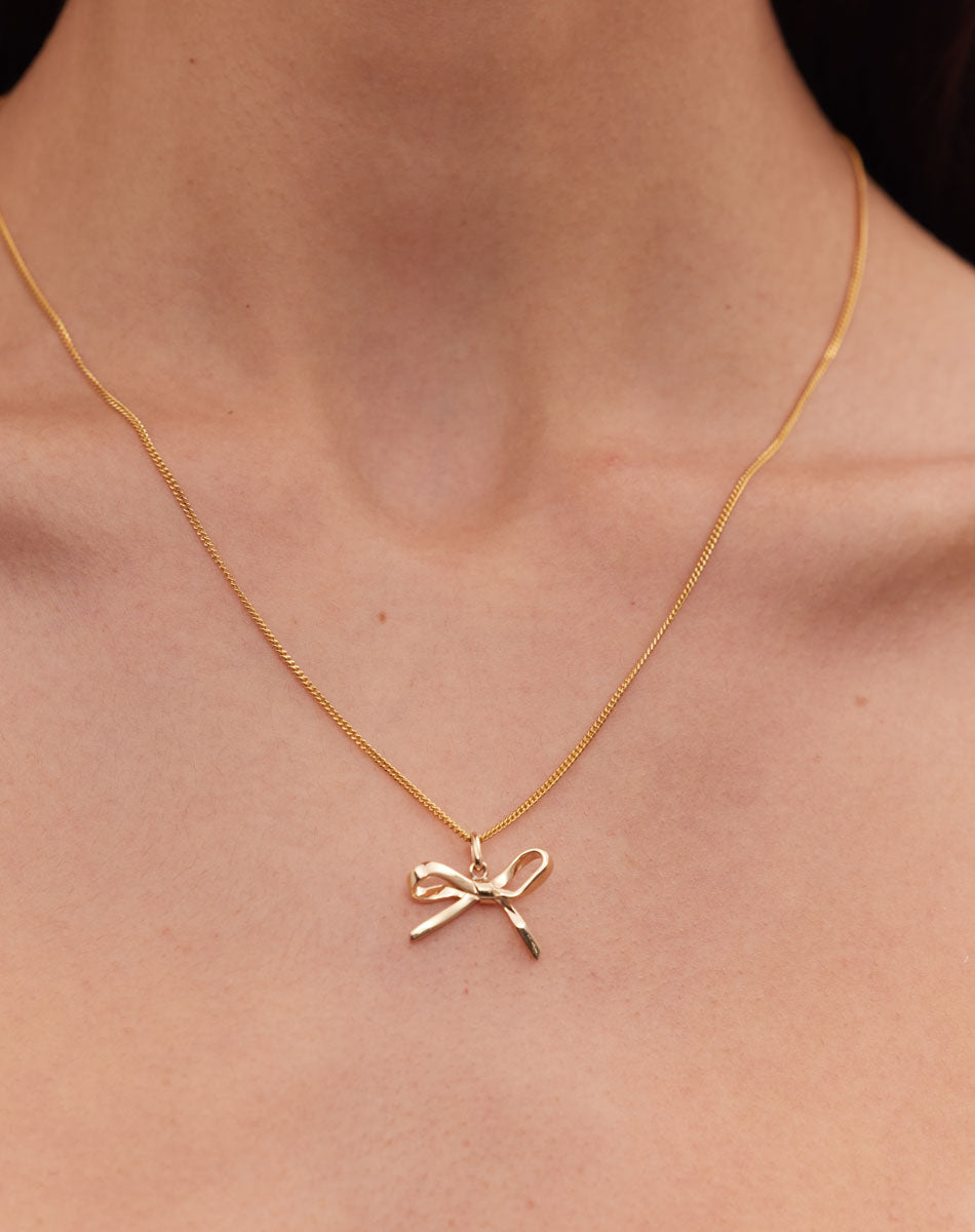 Gold bow charm necklace worn by model