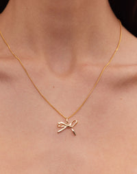 Gold bow charm necklace worn by model
