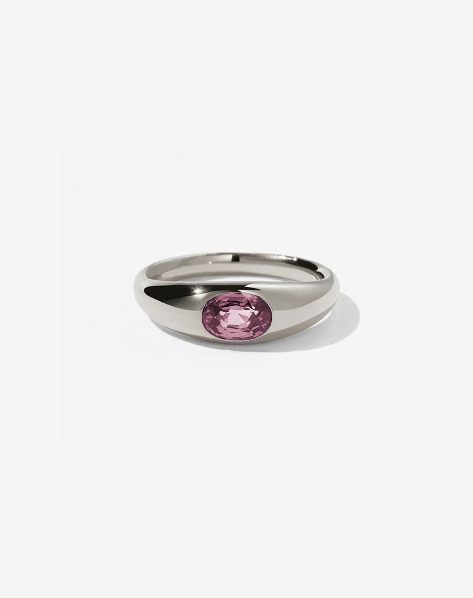 A sterling silver ring with a central oval cut pink tourmaline swiss set in a smooth, rounded band.