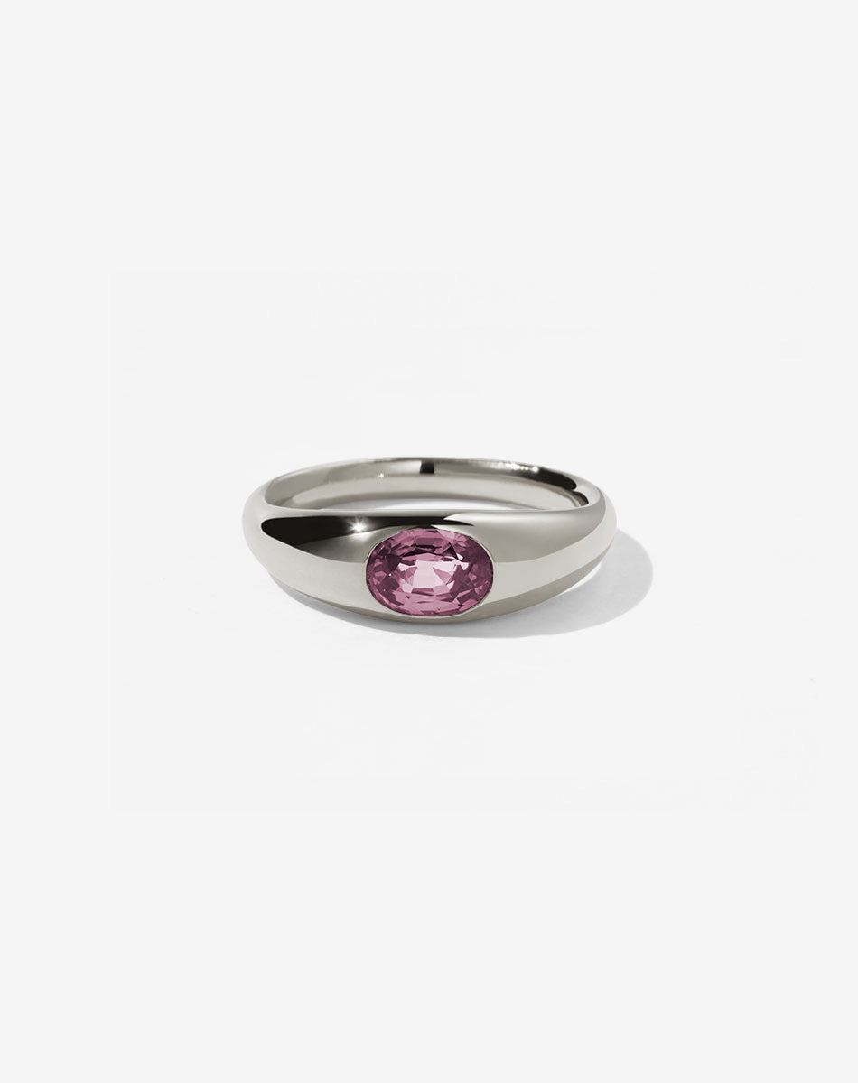 A sterling silver ring with a central oval cut pink tourmaline swiss set in a smooth, rounded band.