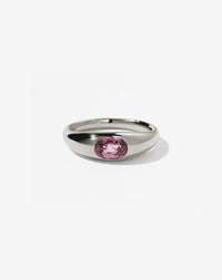 A sterling silver ring with a central oval cut pink tourmaline swiss set in a smooth, rounded band.