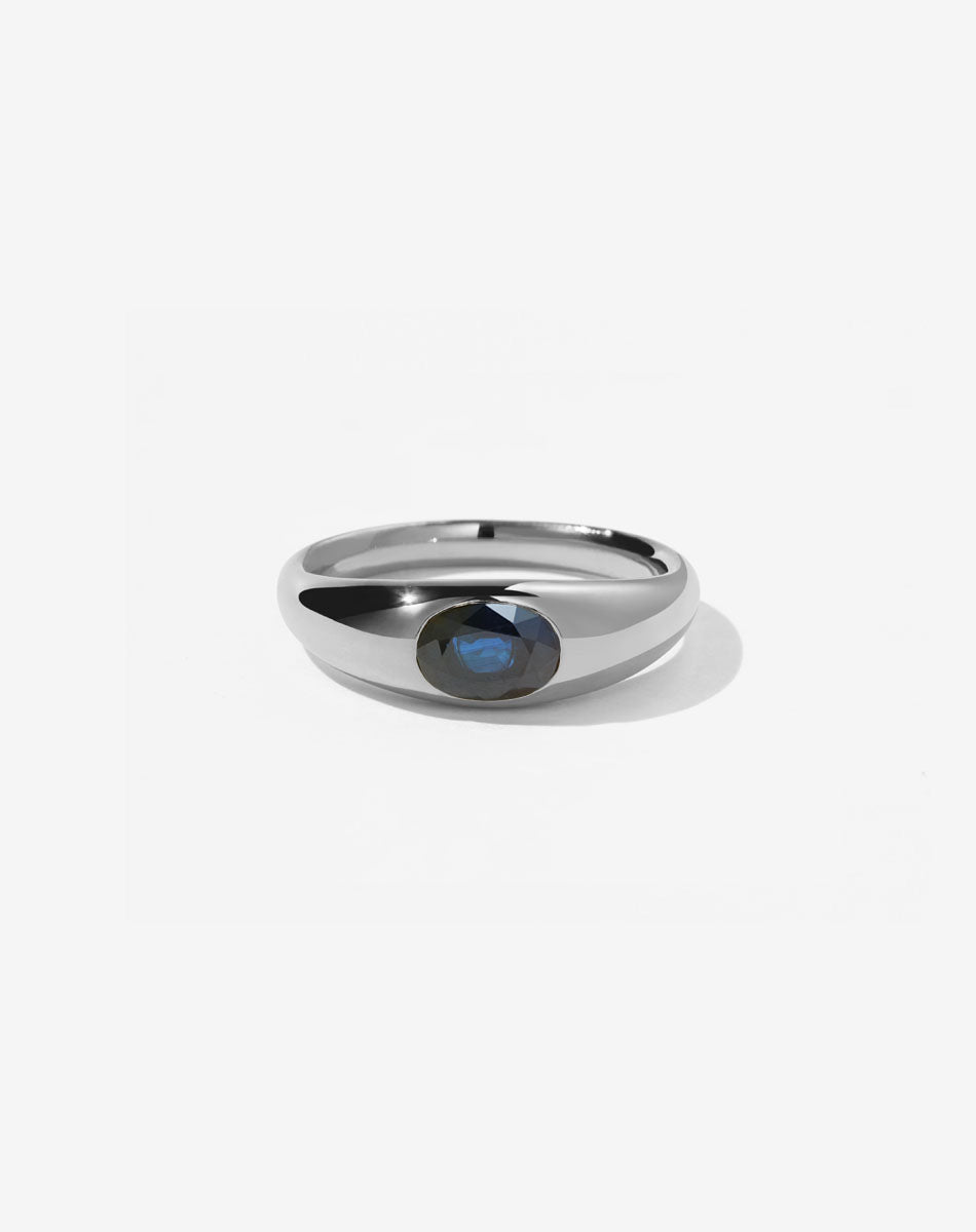 A sterling silver ring with a central oval cut ethical blue sapphire swiss set in a smooth, rounded band.