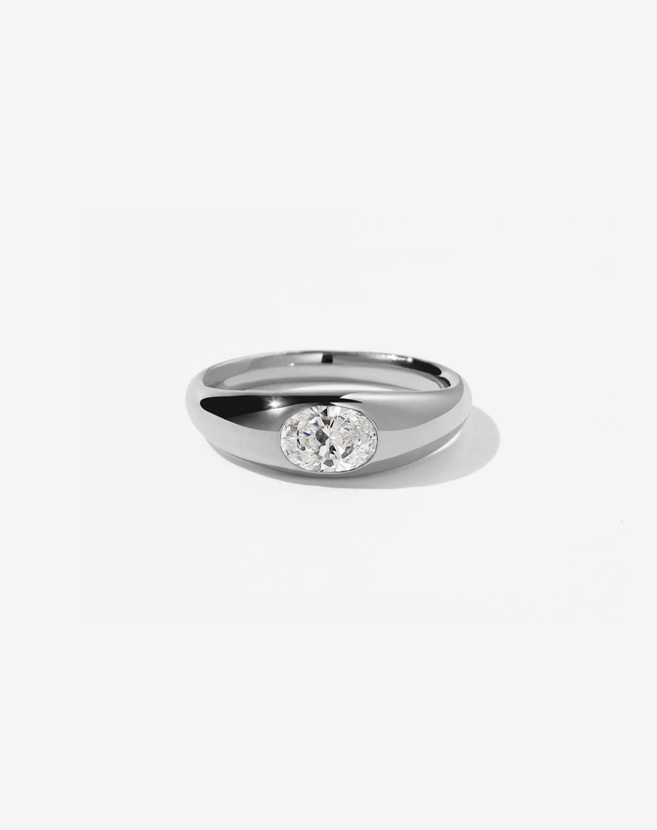 A sterling silver ring with a central oval cut diamond set in a smooth, rounded band.