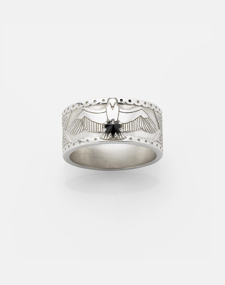 A sterling silver ring featuring a detailed eagle design with a round brilliant stone set in the center, surrounded by a pattern of a Russian orthodox cross and skull etched around the band.