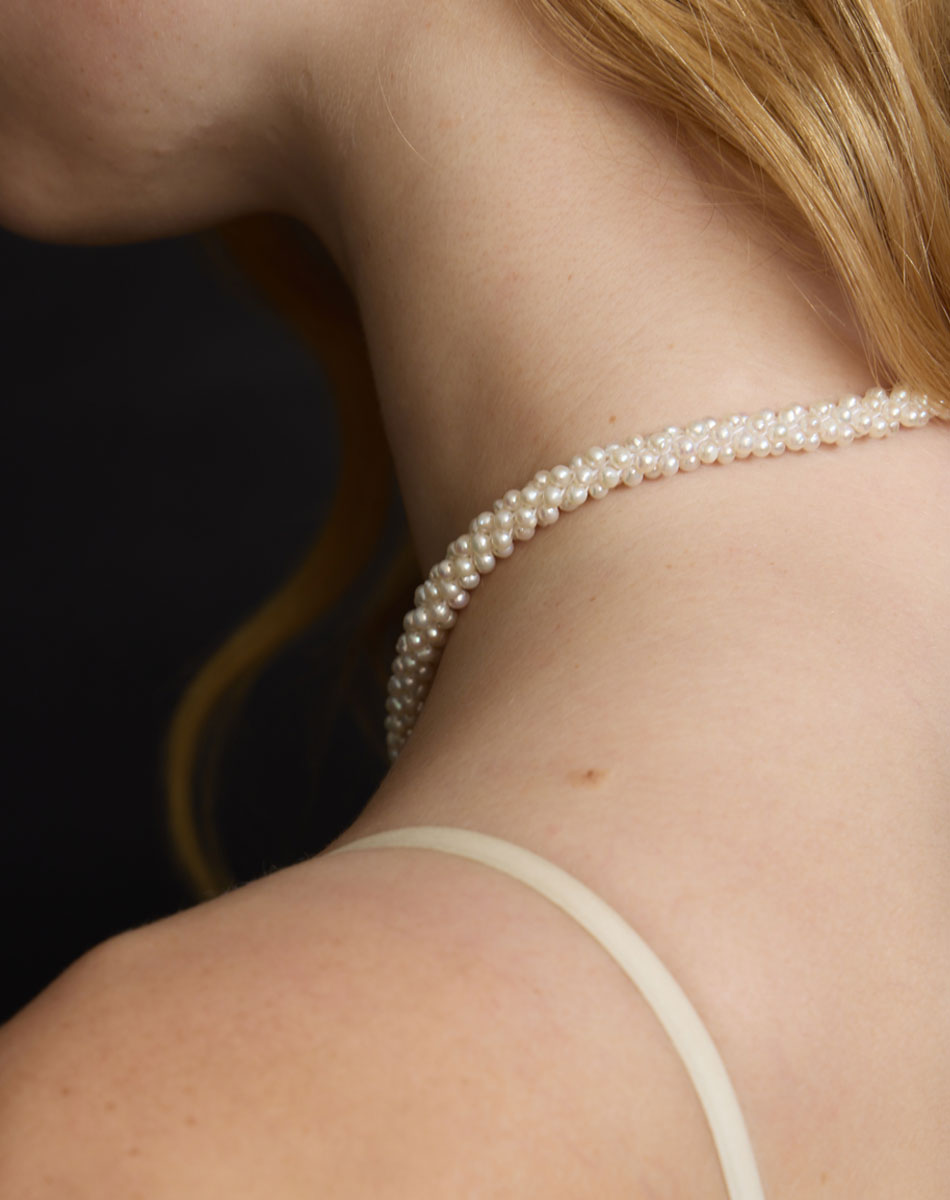 Pearl necklace worn by a person with a dark background