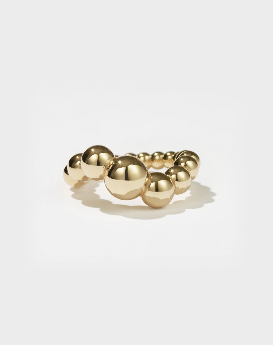 A gold-plated ring with a series of smooth, graduated orbs in graduating size, creating a wave-like pattern on the ring's surface.