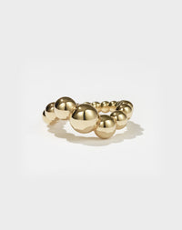 A gold-plated ring with a series of smooth, graduated orbs in graduating size, creating a wave-like pattern on the ring's surface.