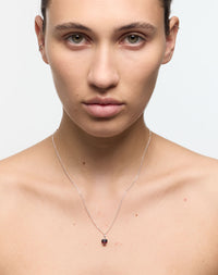 Woman wearing a delicate necklace with a small garnet red, heart shaped gemstone.