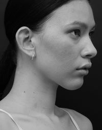 A pair of sterling silver hoop earrings with a central hinge, designed to fit close to the earlobe. Worn on a model