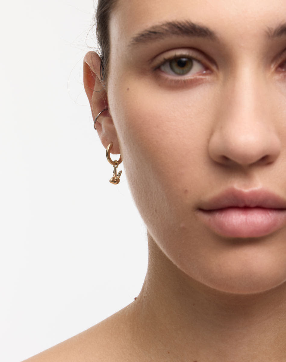 Close-up of a person wearing gold bunny rabbit charm hoop earrings 