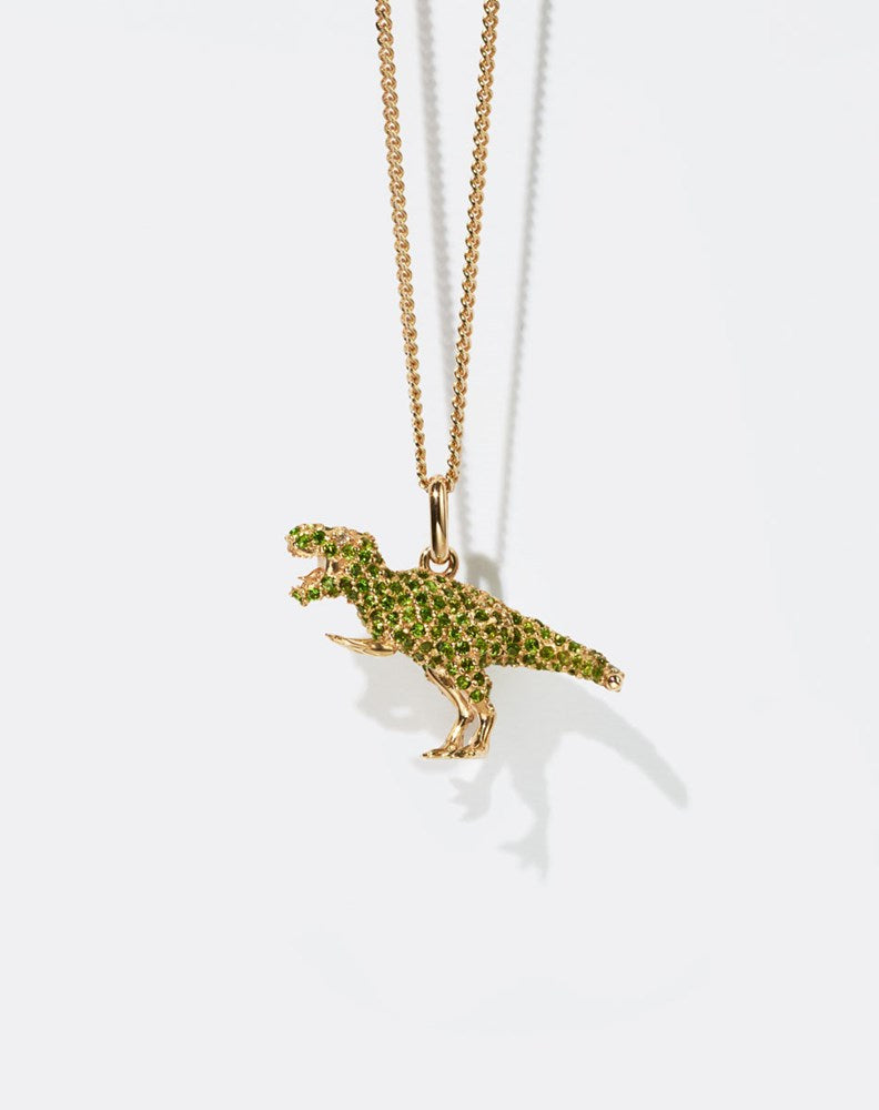 Dinosaur-shaped pendant set with green gemstones on a gold chain against a white background