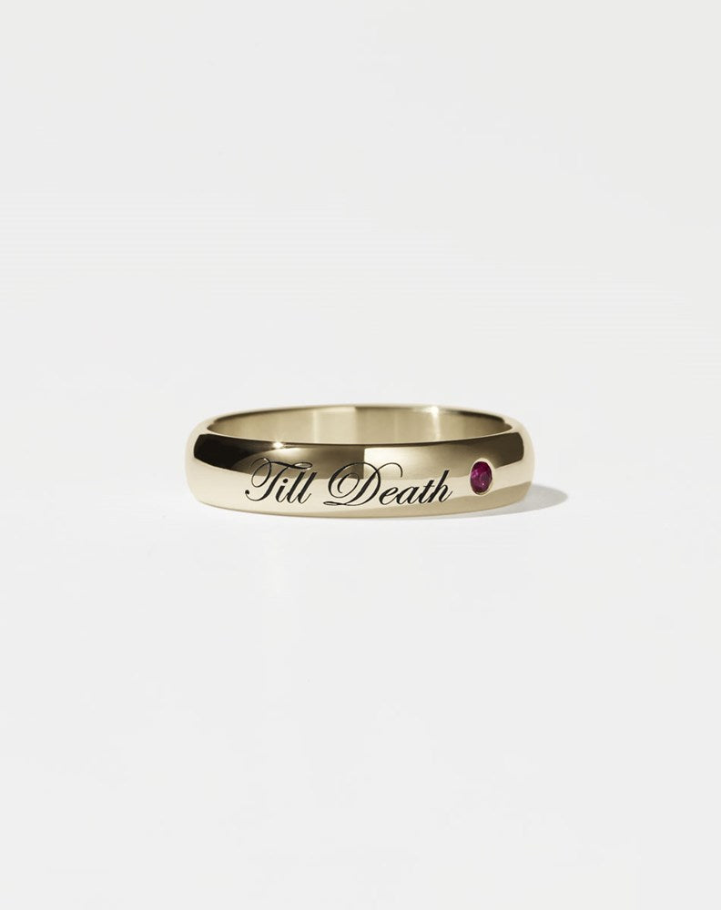 A half-round, yellow gold band ring with the phrase 'Till Death' engraved on it and a small ruby set on one side.
