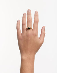 A gold ring with a green emerald worn on a hand with a white background. Made by Meadowlark in New Zealand.