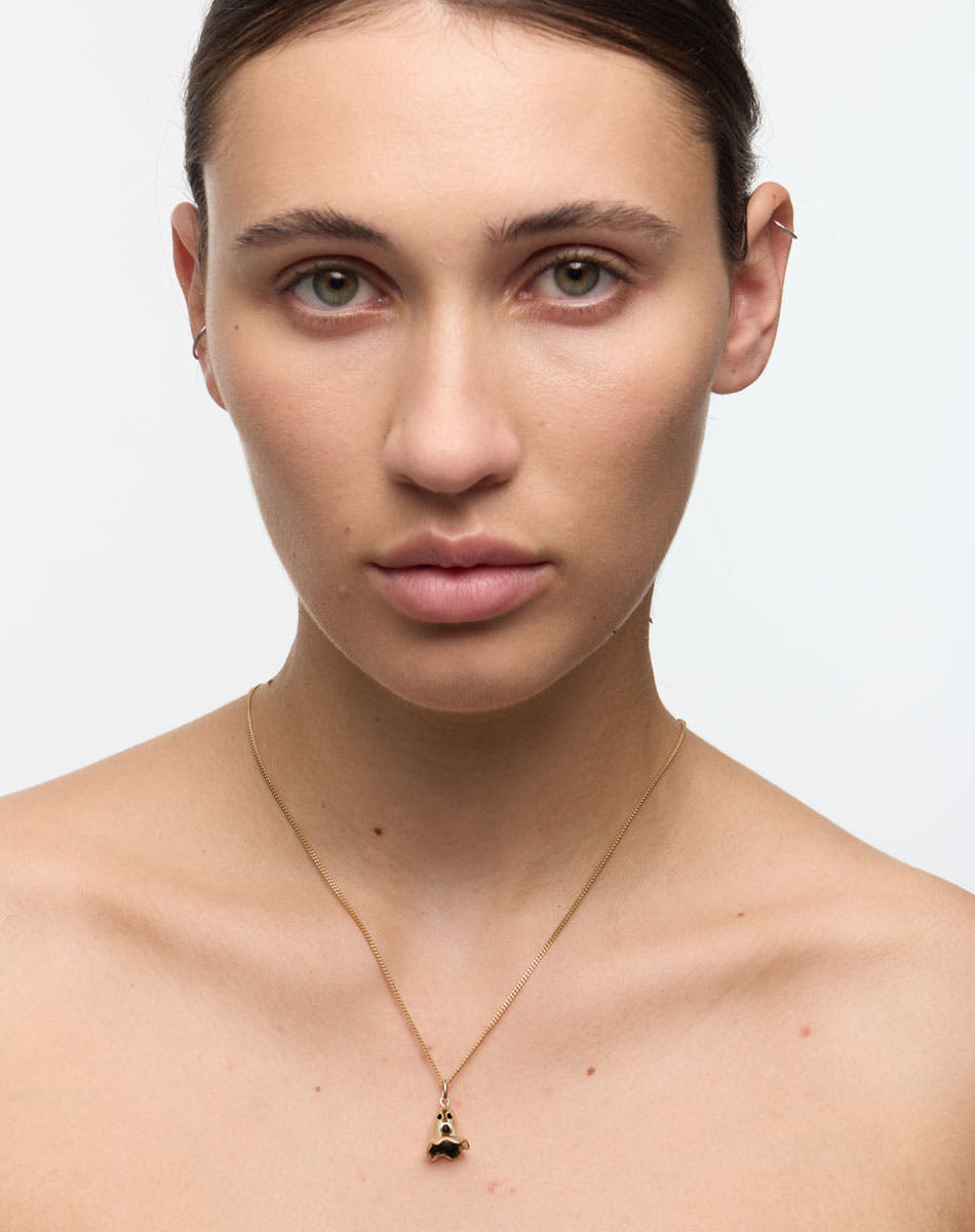 Woman wearing a gold necklace with a ghost pendant. In collaboration with Australian artist Nell