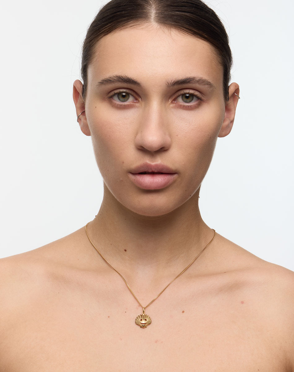 Woman wearing a gold necklace with a shell pendant. A collaboration with Australian Artist Nell