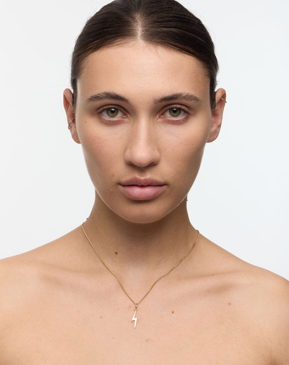 Woman wearing a gold necklace with a small lightning bolt. Thunder bolt necklace