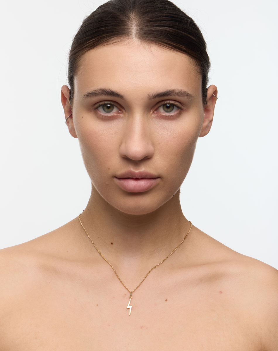 Woman wearing a gold necklace with a small lightning bolt. Thunder bolt necklace