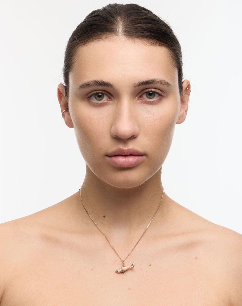 Woman wearing a gold necklace with a shark pendant pavé set with diamonds on a white background