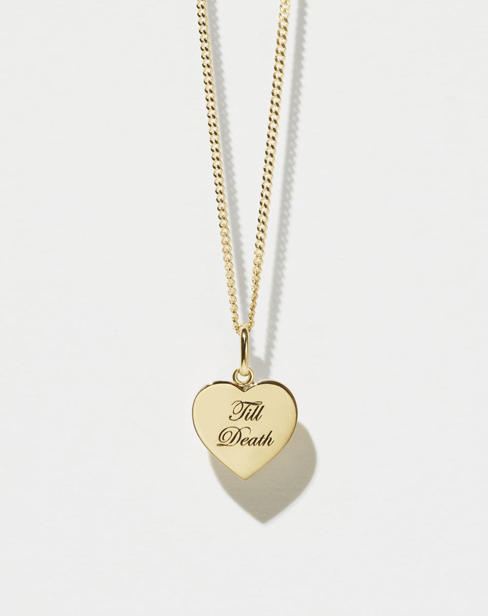 A gold fine chain necklace with a minimalist heart charm that reads 'Till Death'.