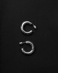 Pair of silver hoop earrings on a black background. 