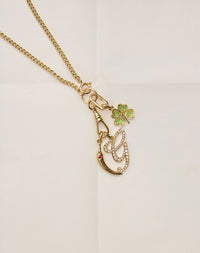 Gold necklace with a pendant featuring a green clover and red gem on a light background