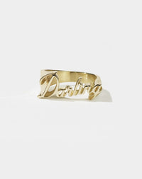 A gold-plated, flat-top knuckle duster style ring with the word 'DARLING' in cursive script.