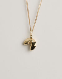 Gold necklace with a lucky fortune cookie pendant on a light grey background