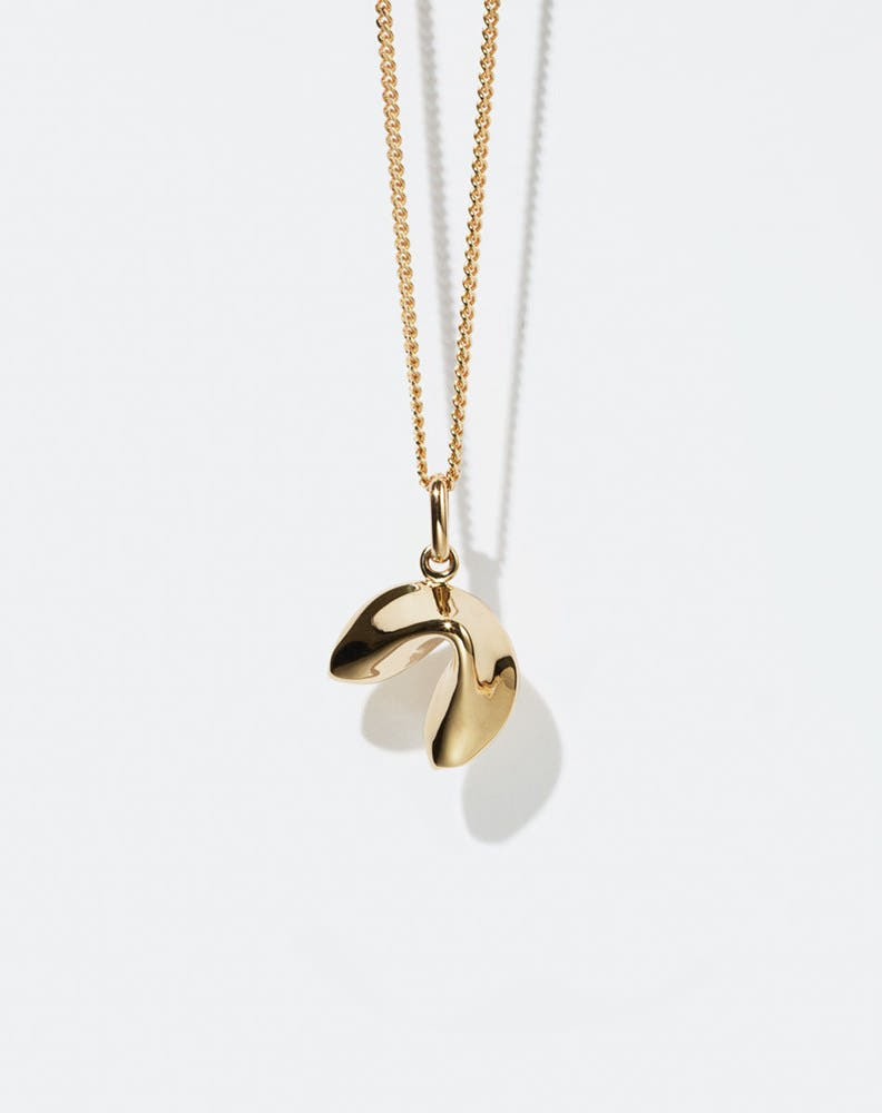 Gold necklace with a fortune cookie shaped pendant on a white background