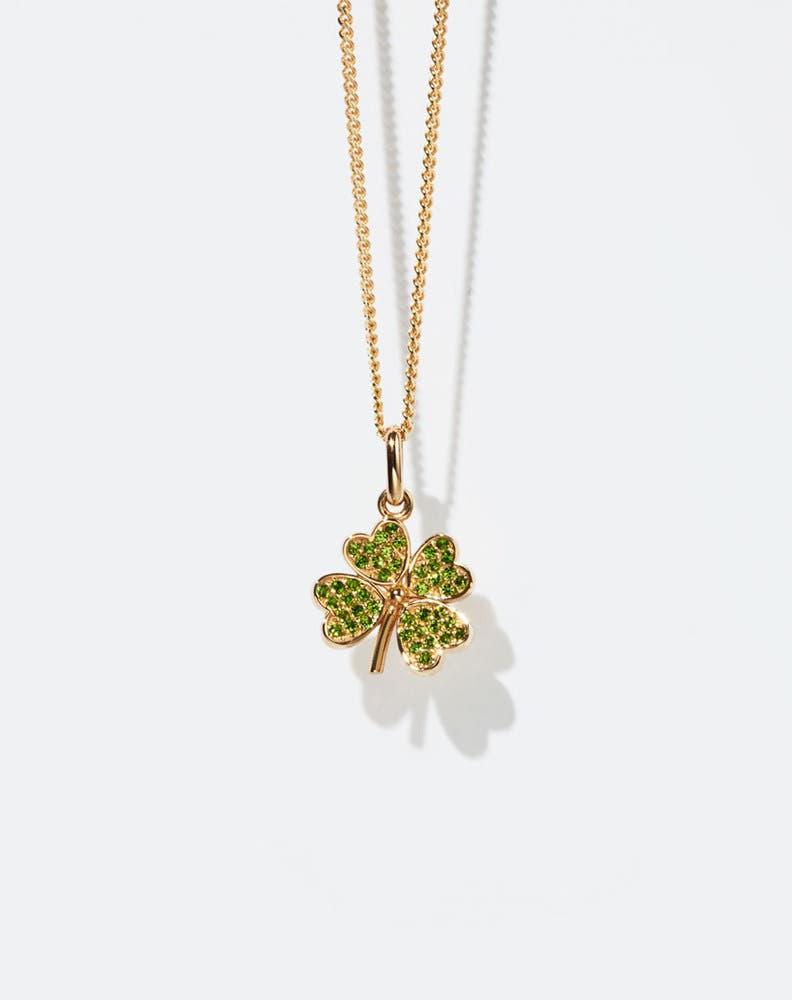 Gold necklace with a four-leaf clover pendant set with green gemstones on a white background