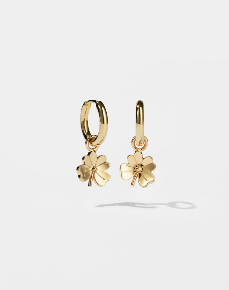 Gold hoop earrings with for leaf clover charms on a light grey background