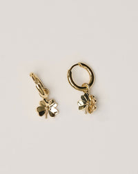 Gold hoop earrings with four-leaf clover charms on a light beige background