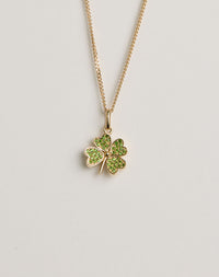 Gold necklace with a four-leaf clover pendant set with green gemstones on a light grey background
