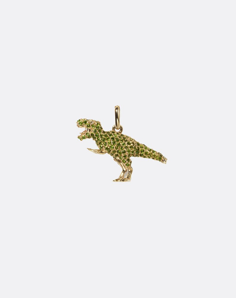 Gold pendant shaped like a dinosaur and set with green gemstones on a white background