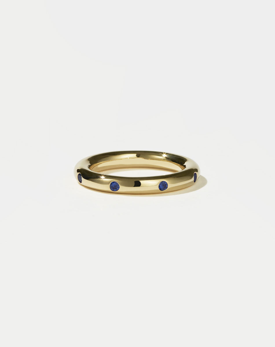 Gold ring with blue sapphires on a light gray background
