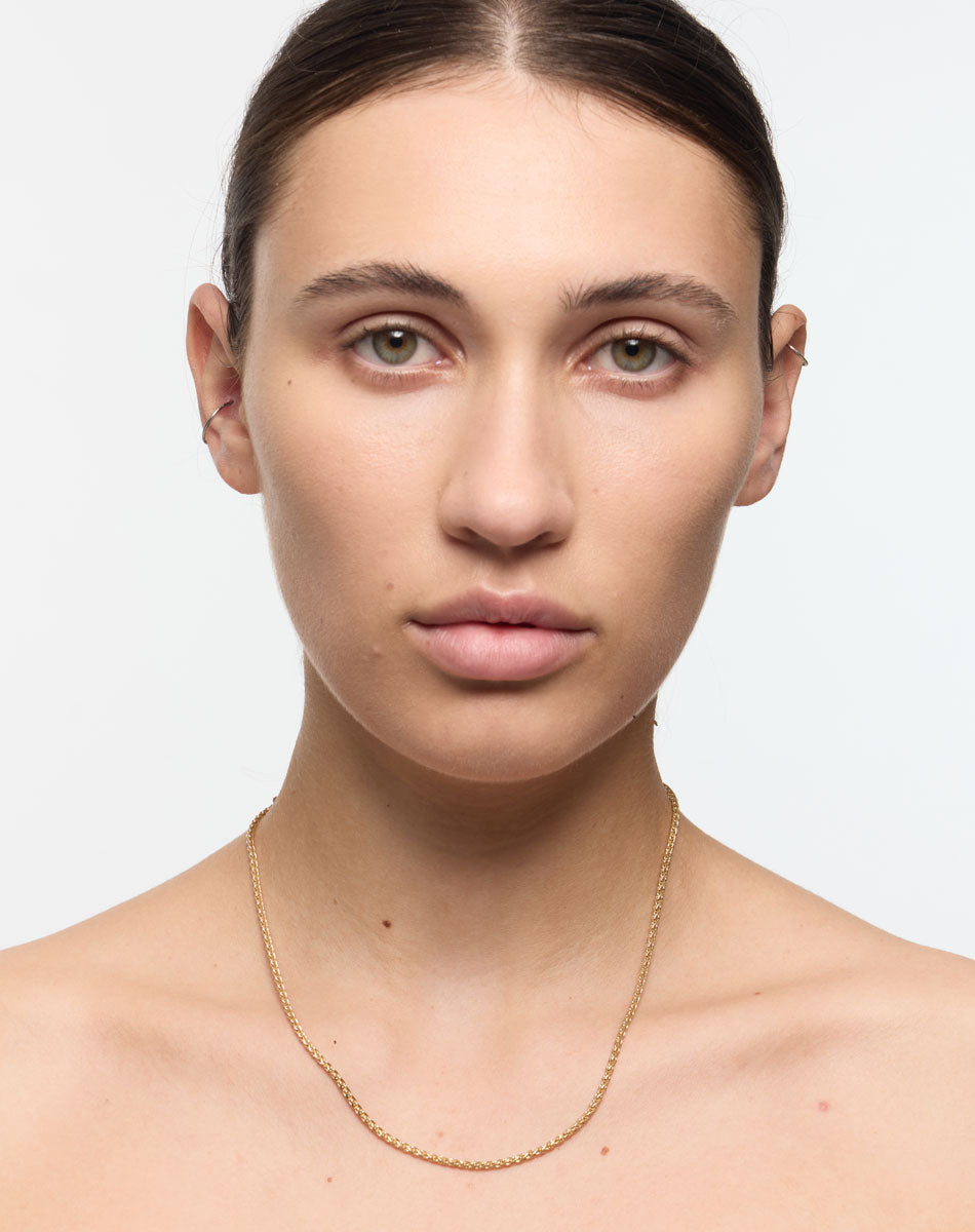 Woman wearing a gold necklace against a plain background