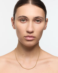 Woman wearing a gold necklace against a plain background