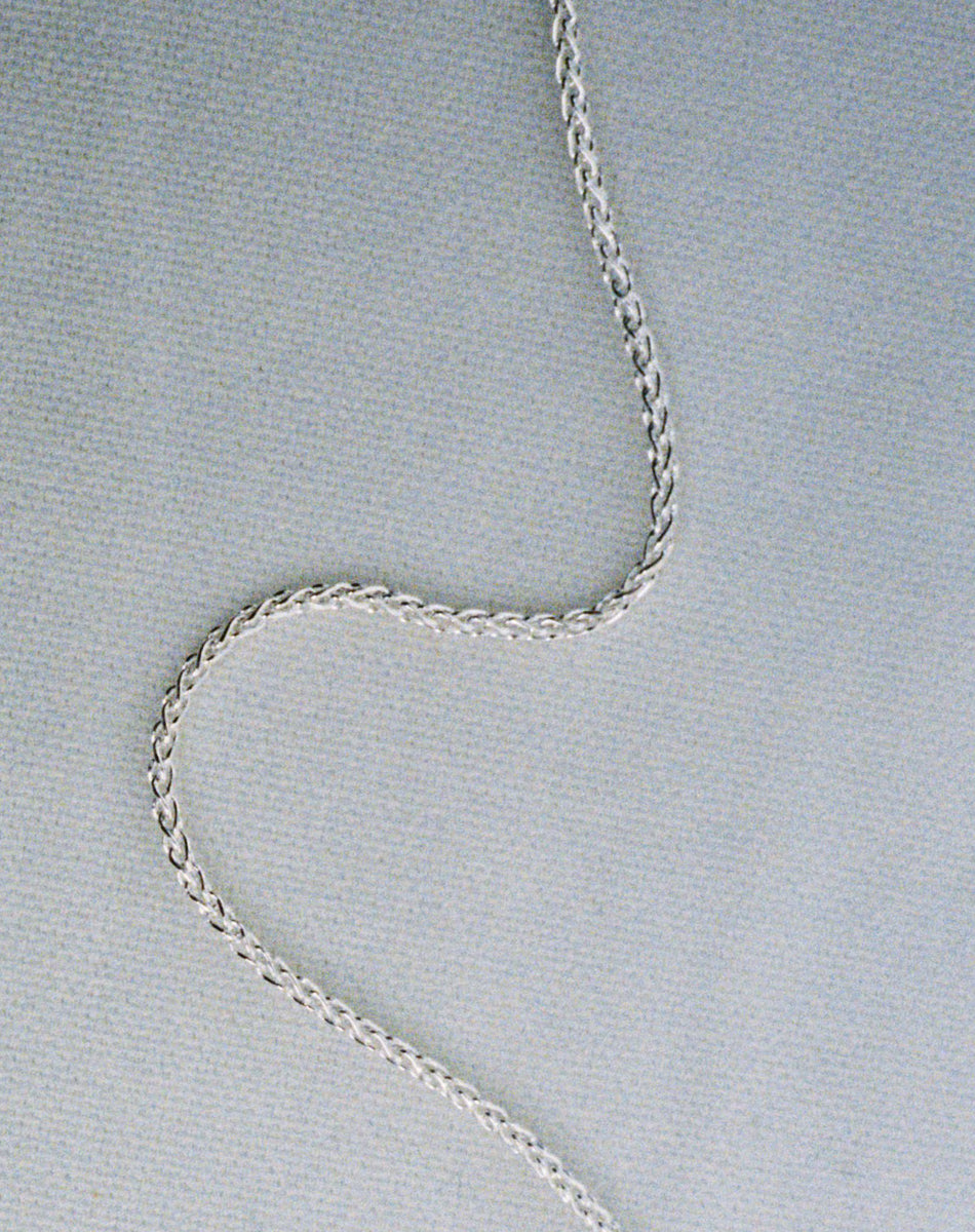 A silver wheat chain necklace on a textured background.