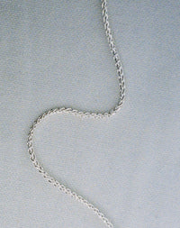 A silver wheat chain necklace on a textured background.