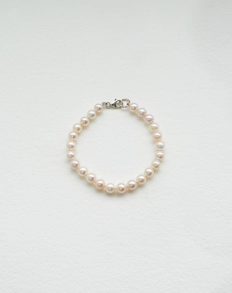 A bracelet featuring round freshwater pearls strung on silk thread with sterling silver clasp.