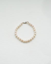 A bracelet featuring round freshwater pearls strung on silk thread with sterling silver clasp.