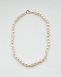A freshwater pearl necklace with a classic round pearl design, strung on a silk thread and knotted.