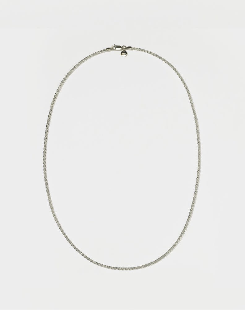 A sterling silver wheat chain necklace laid out on a plain surface.