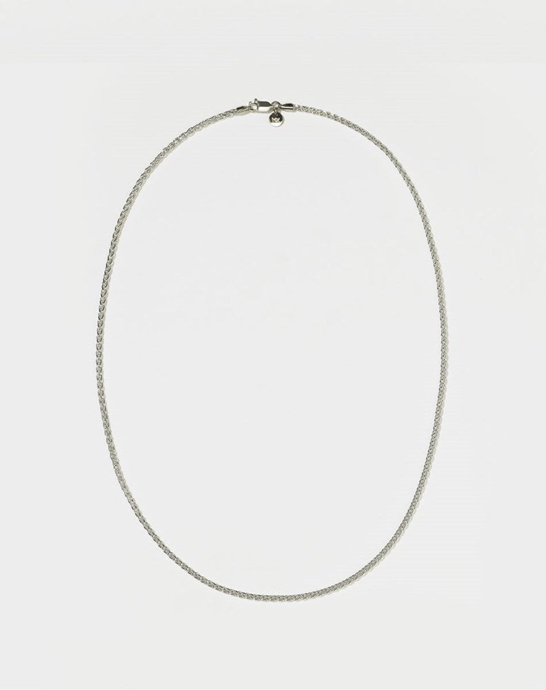 A sterling silver wheat chain necklace laid out on a plain surface.