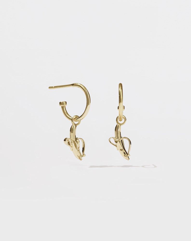 A pair of gold hoop earrings with a small gold-colored banana charm hanging from each hoop.