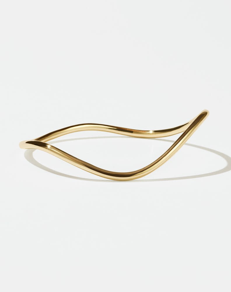 A gold-plated bracelet with a flat, minimalist design and an organic, curvy shape.